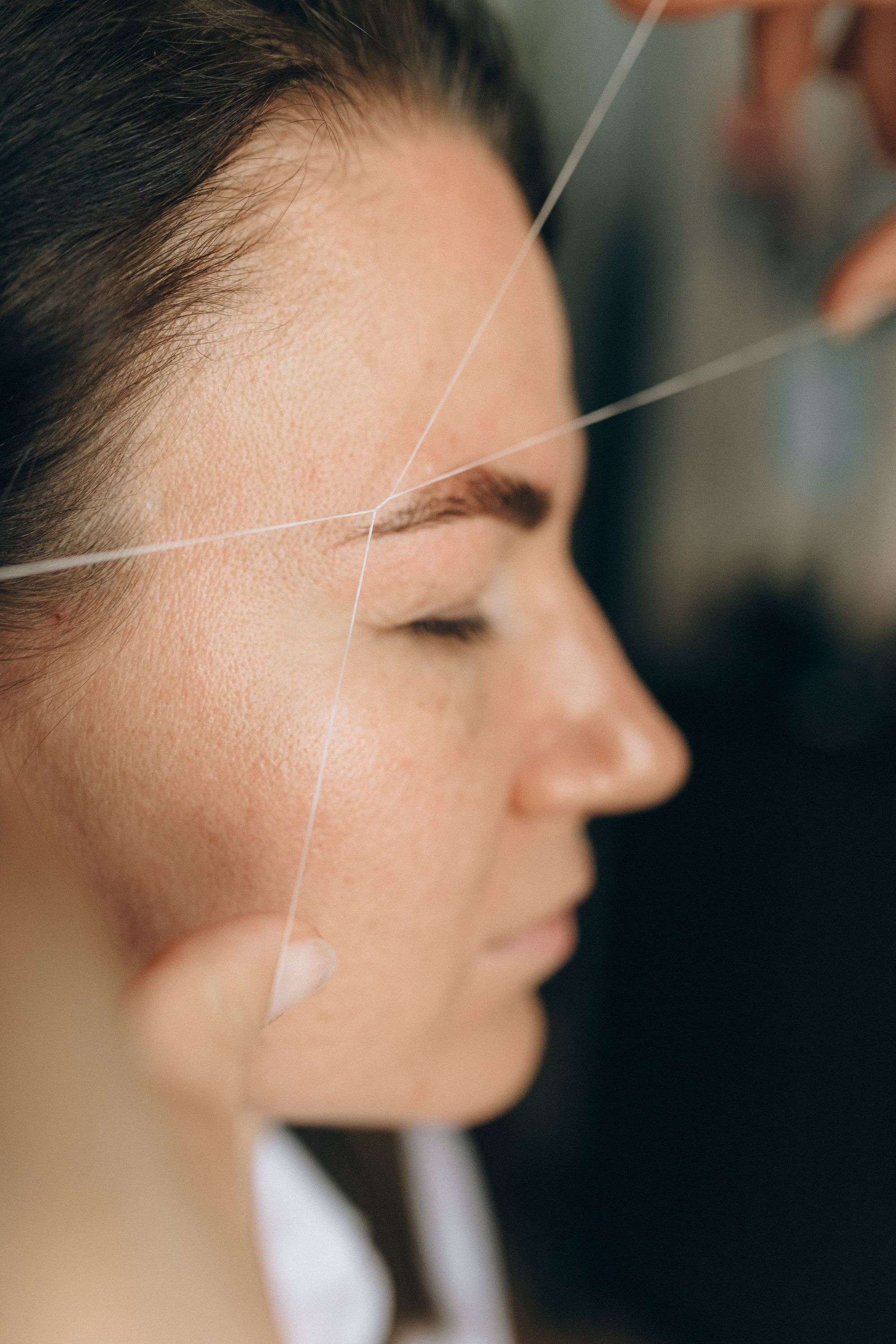 Side view of a guest receiving precise cotton-thread eyebrow shaping